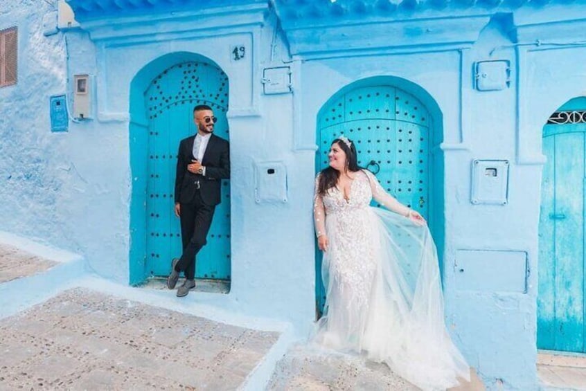 A man in a black suit and a woman in a white wedding dress standing in front of turquoise doors. 1