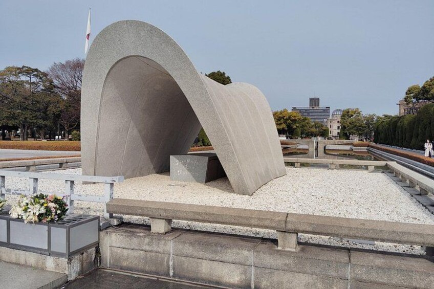 Een betonnen monument met een gebogen bovenkant, omgeven door grind en een klein bloemstuk. 5