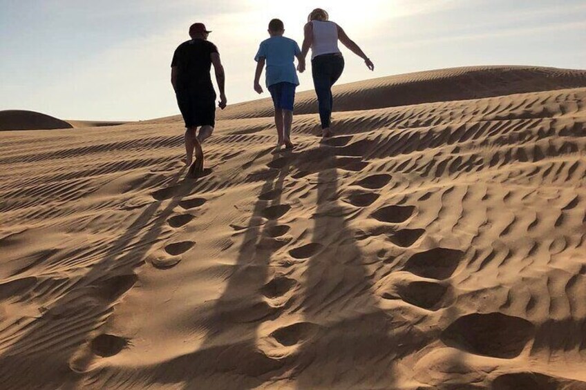 Zwei Personen laufen durch eine sandige Wüstenlandschaft, Fußspuren im Sand. 3