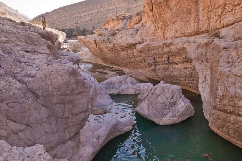 Eine felsige Schlucht mit einem schmalen Wasserlauf und einer Person, die auf einem Felsen steht. 4