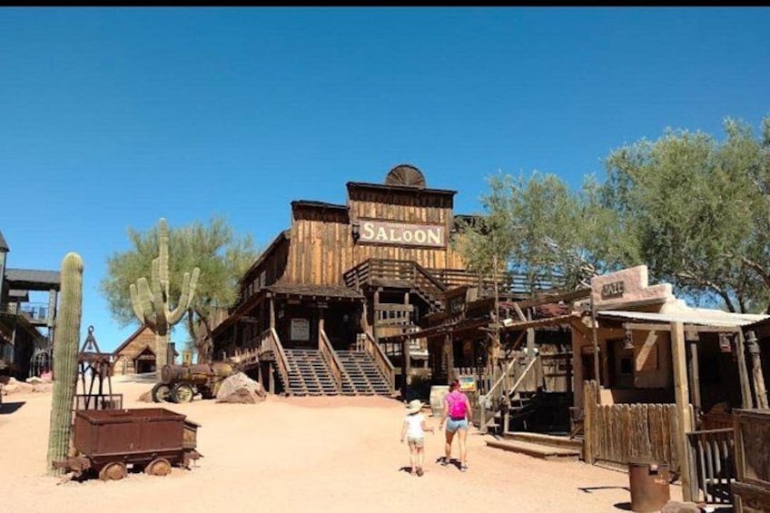 A wooden building labeled 'Saloon' with a desert landscape, cacti, and a wooden cart. 4