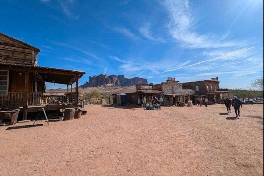 A desert town with wooden buildings, a clear blue sky, and mountains in the background. 3