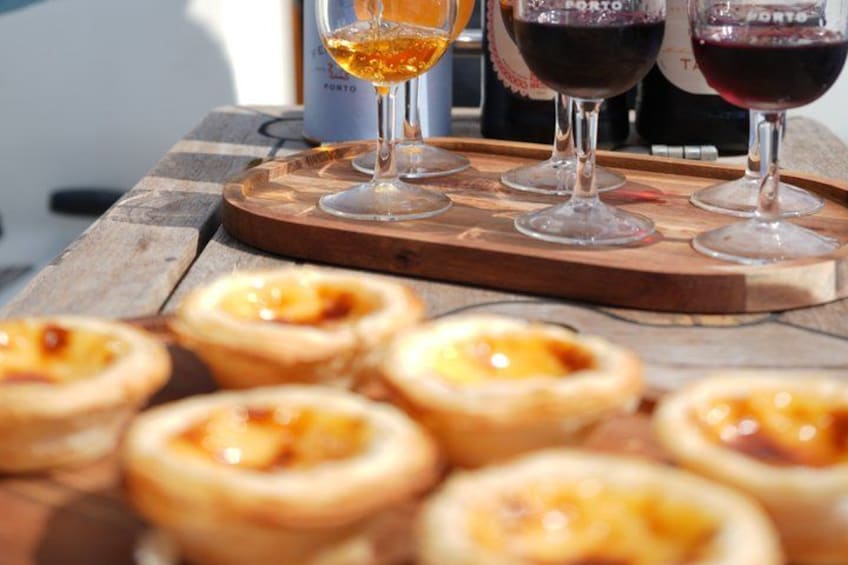 Een houten tafel met diverse kleine gebakjes en twee glazen wijn. 1