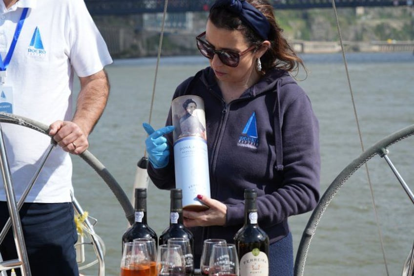 Een persoon houdt een fles en blikje vast op een boot, met flessen en glazen op het dek. 4