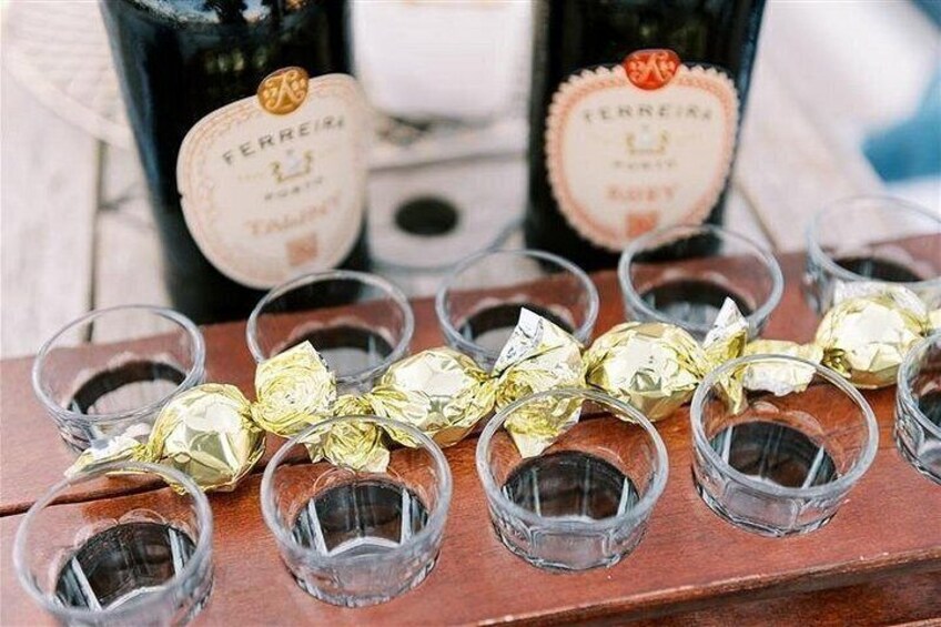Een houten dienblad met shotglazen en ingepakte chocolade, met twee flesjes met de naam 'Ferreira' op de achtergrond. 4