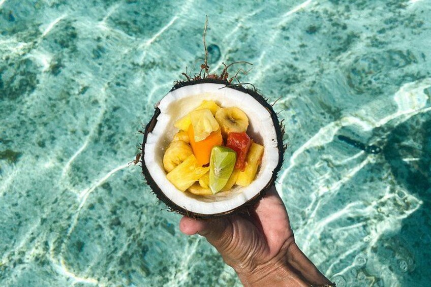 A hand holding a coconut filled with pineapple, banana, and lime. 4