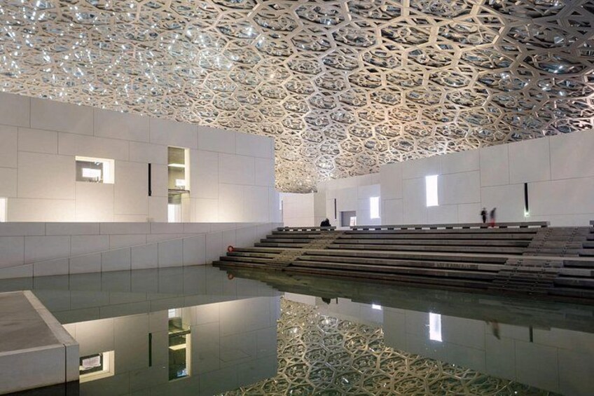 Un interior arquitectónico moderno con piso reflectante, diseño geométrico en el techo y una escalera central. 2