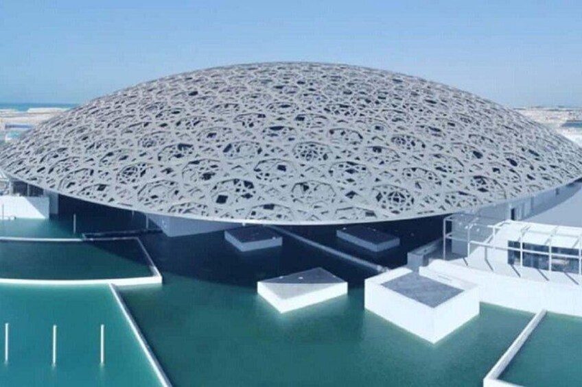 Un edificio grande y circular con techo perforado, rodeado de agua y cielo despejado. 5