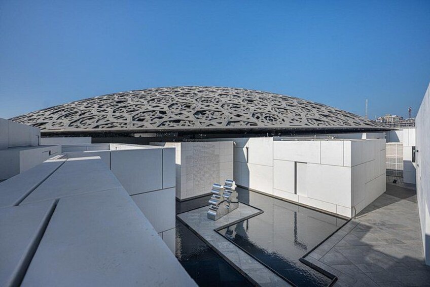 Una estructura arquitectónica moderna con techo estampado y un elemento acuático reflectante. 3