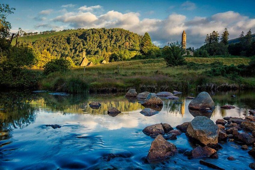 Een rivier met grote rotsen, een bebost heuvel, en een toren in de verte. 1