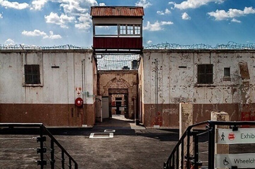 Un edificio con una torre di guardia, filo spinato e un cartello che indica l'accessibilità per disabili. 3