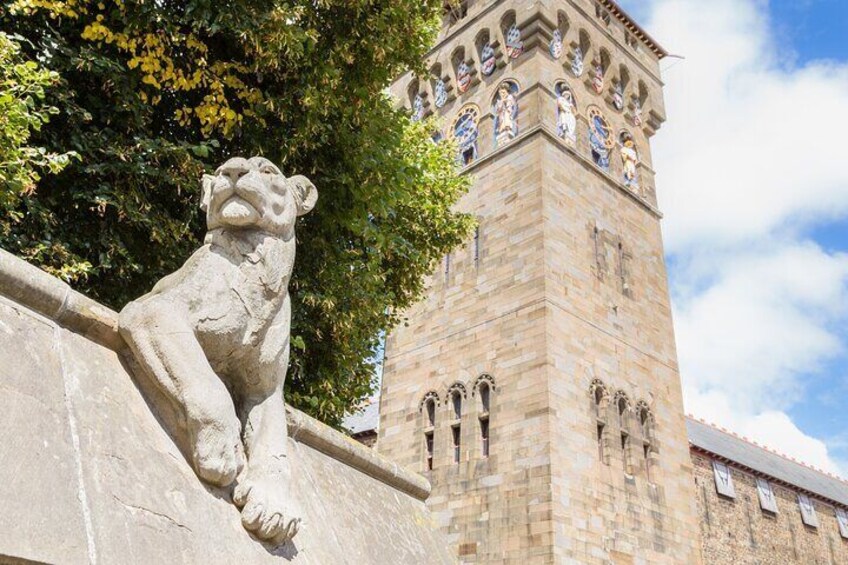 Una estatua de león de piedra frente a una torre alta con ventanas de arco y un reloj. 4