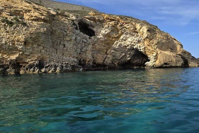 Un litoral rocoso con agua azul cristalina y la entrada de una cueva. 4