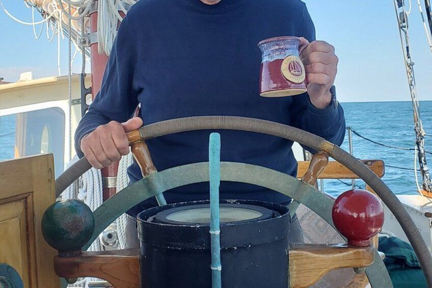 Una persona manejando un bote, sosteniendo una taza, con un timón y un contenedor grande al frente. 5