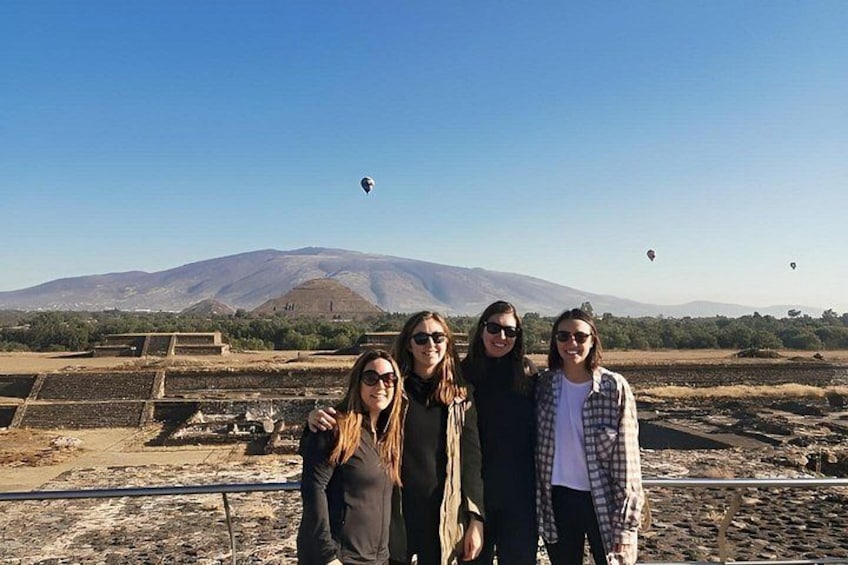 A group of people standing outdoors with a mountainous landscape and hot air balloons in the background. 2