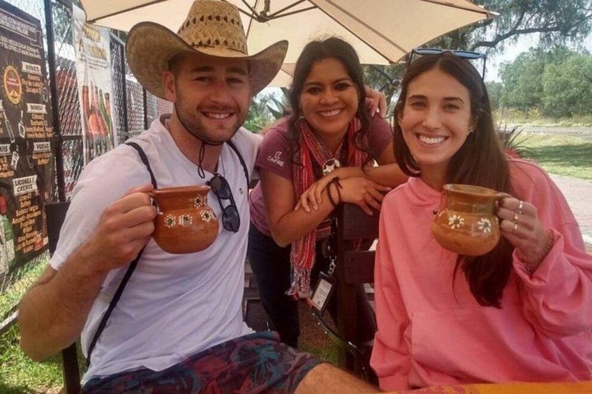 Three people holding pottery cups, sitting under an umbrella. 4