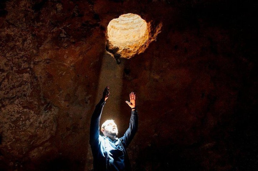 A person reaching up towards a glowing object in a cave. 5