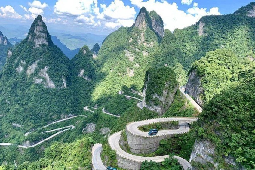 A winding mountain road with a car on a curve, surrounded by lush green forests and towering cliffs. 5