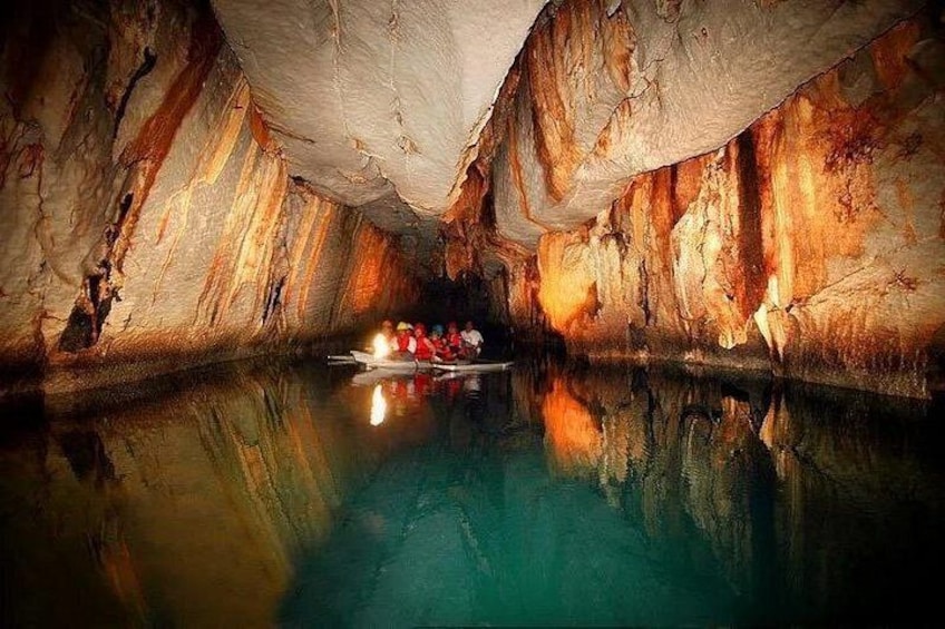 Une grotte ornée de stalactites et de stalagmites, un bateau rempli de personnes et une surface d’eau qui reflète la lumière. 1