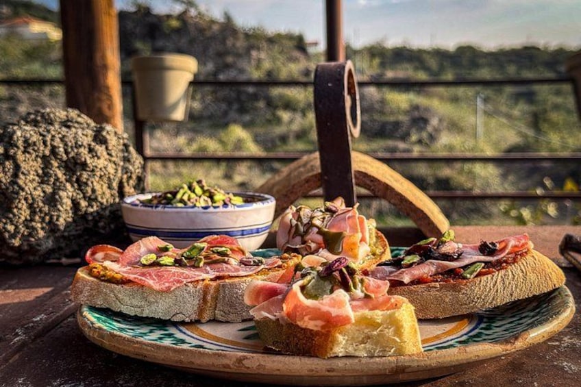 Un entorno rústico al aire libre con una mesa de madera, una fuente de bruschetta y un bol de aceitunas. 4