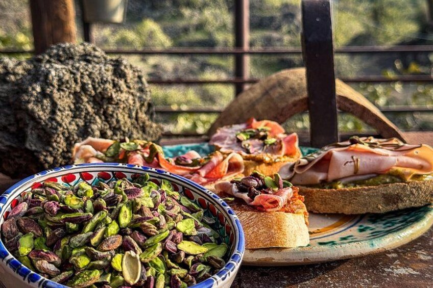 Un entorno rústico al aire libre con una mesa de madera, un cuenco de pistachos y un plato con diferentes alimentos. 5