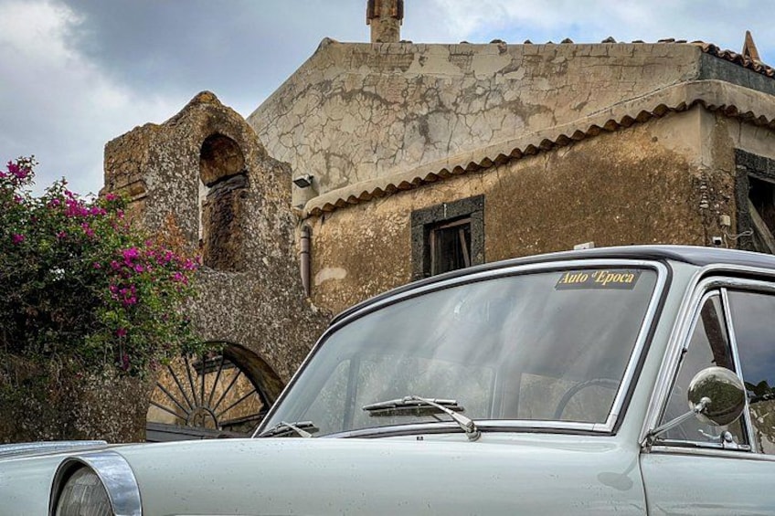 Un coche antiguo estacionado frente a un edificio histórico con fachada desgastada y una gran estructura circular. 3