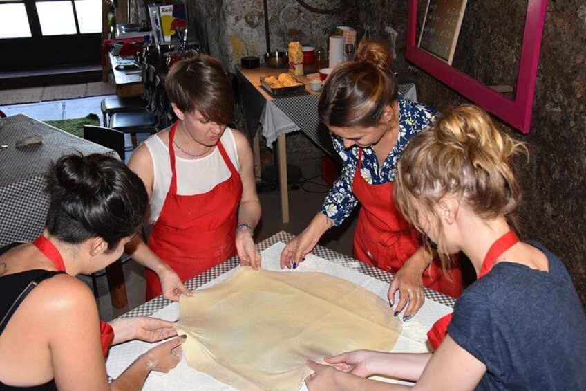 Cuatro personas con delantales trabajando juntas en una mesa con una gran lámina de masa. 2