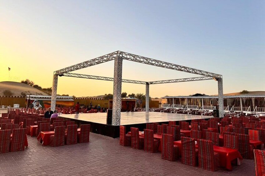 An outdoor event with a stage and red chairs arranged in rows. 2