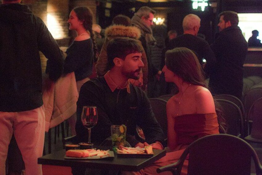 A restaurant with people dining, a man and a woman at a table, and a wine glass on the table. 2