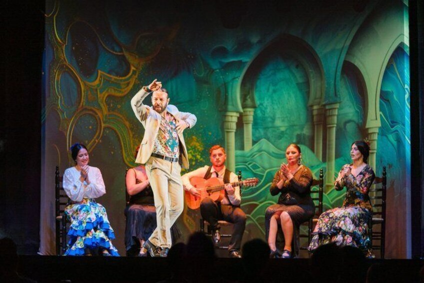 A stage performance with actors in period costumes, a guitar player, and a backdrop with arches and abstract designs. 3