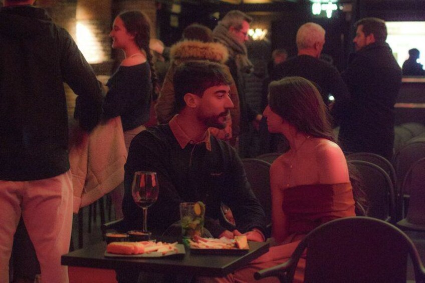 Ein Restaurantambiente mit Gästen, einem Tisch mit Essen und einem Weinglas, und gedämpftem Licht. 3
