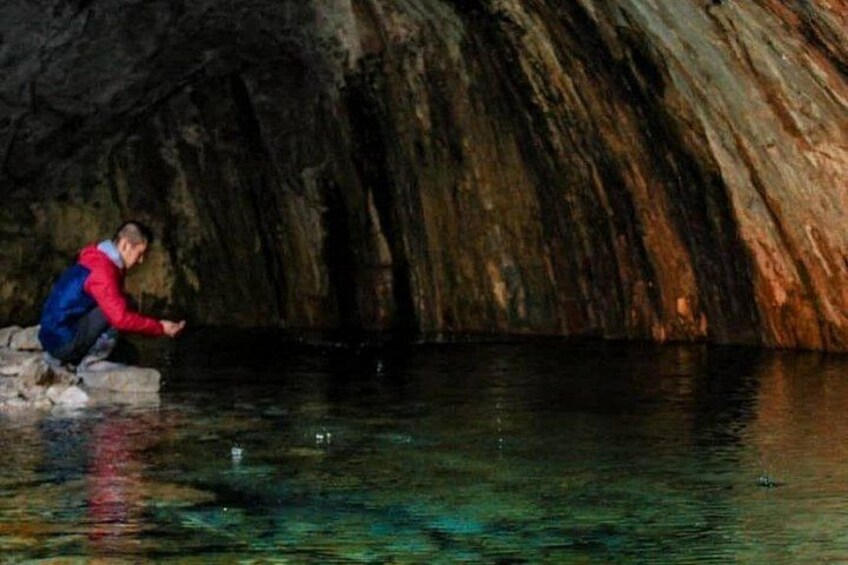En person hukar sig vid en klar vattenyta inuti en grotta med steniga väggar. 3