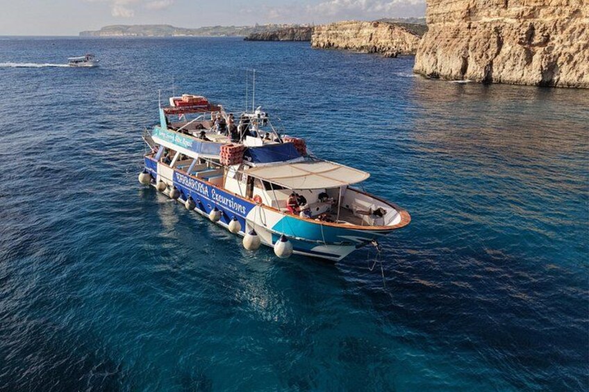 Una barca chiamata 'La Vita Nuova' su un mare blu e limpido, con scogliere rocciose sullo sfondo. 3