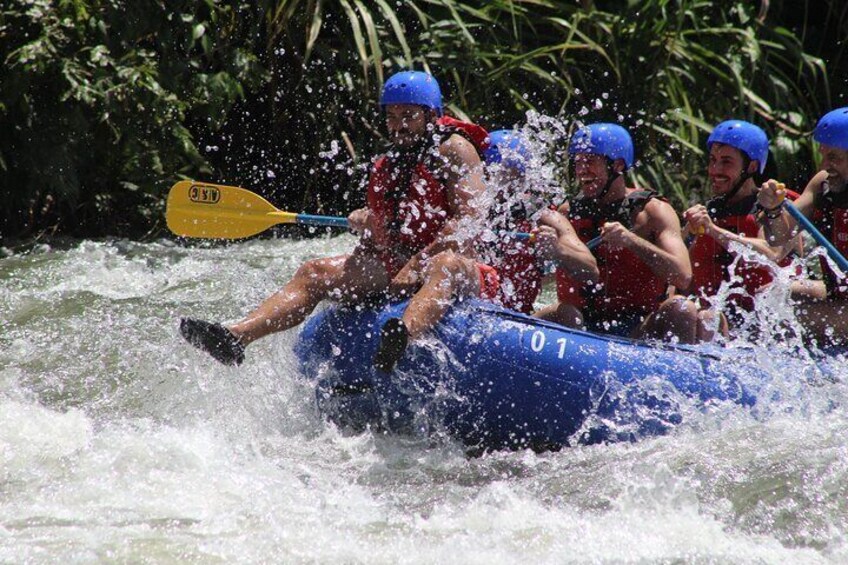 A group of people in a blue raft navigating through a river, wearing helmets and life jackets. 5