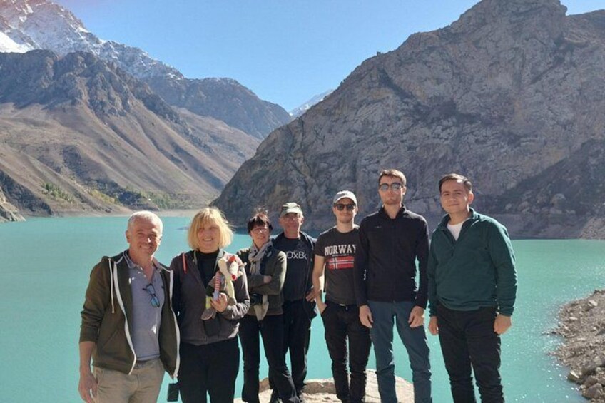 Eine Gruppe von Menschen steht an einem türkisblauen See mit Bergen im Hintergrund. 3