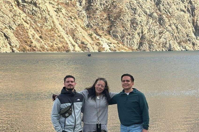 Drei Personen stehen an einem See, im Hintergrund eine felsige Klippe. 2