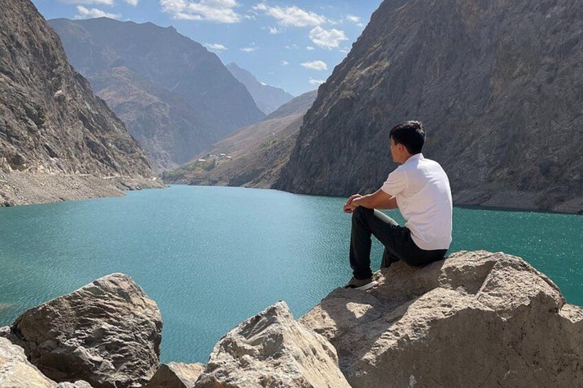 Eine Person sitzt auf einem Felsen an einem türkisblauen See, umgeben von Bergen. 4