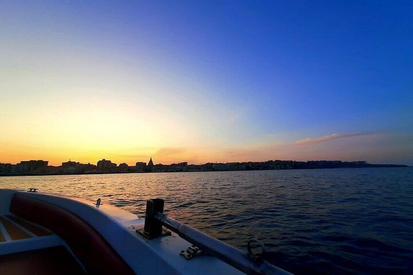 Een zonsondergang boven het water, met een stadszicht op de achtergrond. 1