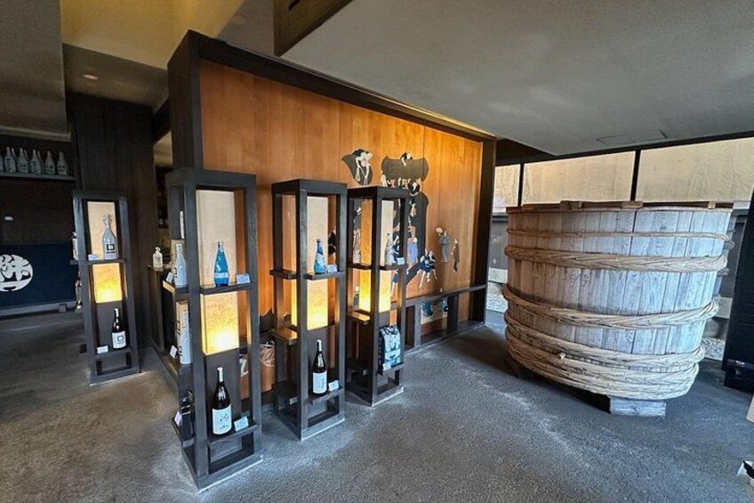 A bar with wooden shelves displaying bottles and a large wooden barrel. 2