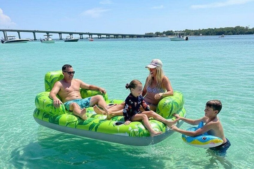 A family on a green inflatable raft in clear turquoise water with a pier in the background. 2