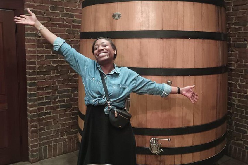 A person standing in front of a large wooden barrel with arms outstretched. 2
