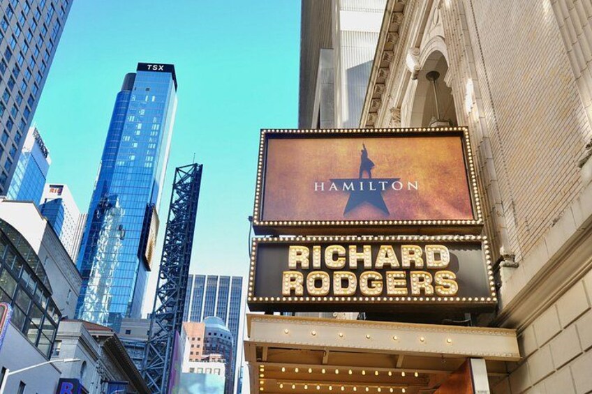 A theater marquee with 'Hamilton' and 'Richard Rodgers' written on it, set against a cityscape with tall buildings. 5