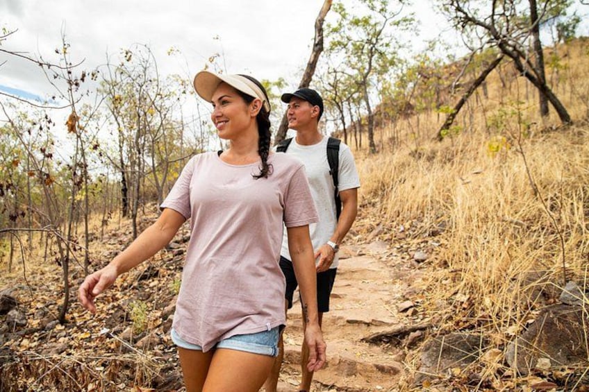 Two people hiking on a dirt trail surrounded by dry vegetation and sparse trees. 3