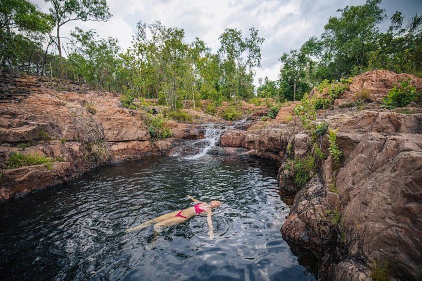 A person swimming in a natural pool surrounded by rocky terrain and trees. 4