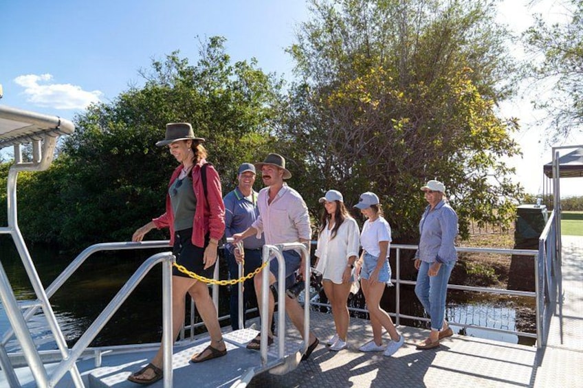 A group of people on a dock near water, with trees and a clear sky in the background. 2