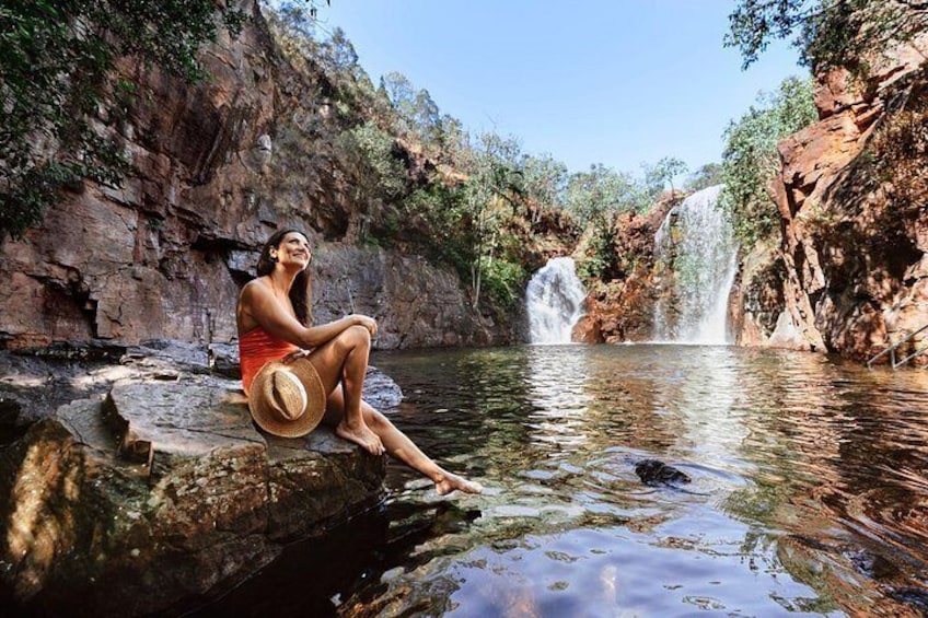 A person sitting on a rock by a waterfall in a natural setting. 2