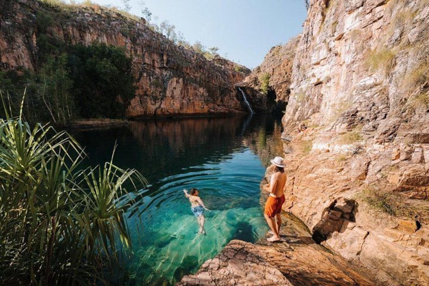 A person standing on a rock by a clear blue water body with a cliff in the background. 3