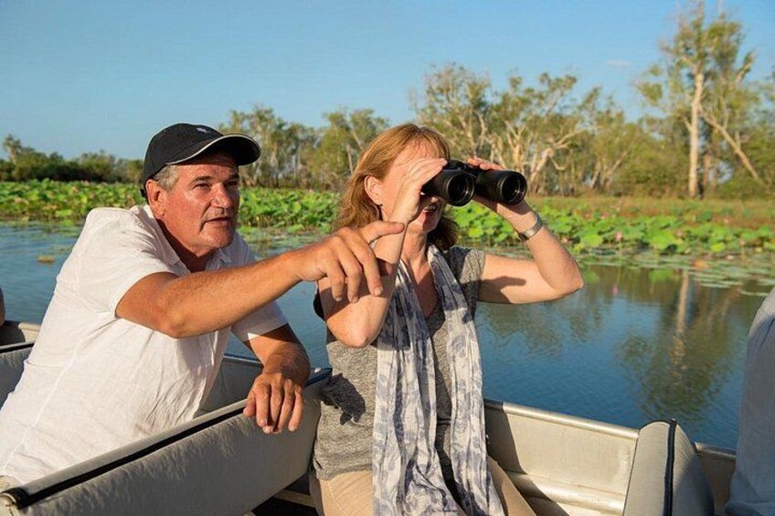 Two people on a boat, one pointing binoculars at the water. 5