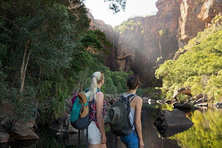 Two people hiking in a canyon with a river and greenery. 1