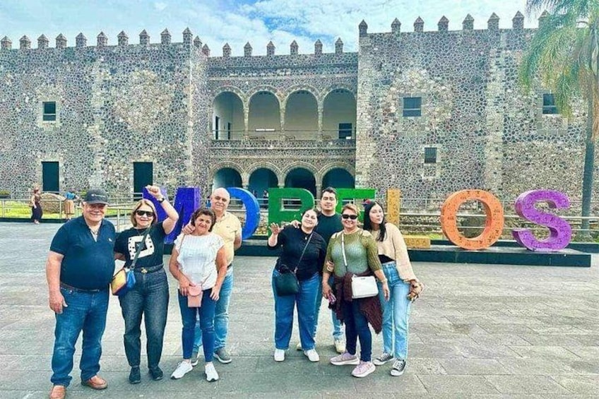 A group of people in front of a historic stone building with large letters spelling 'LOS' in the foreground. 2